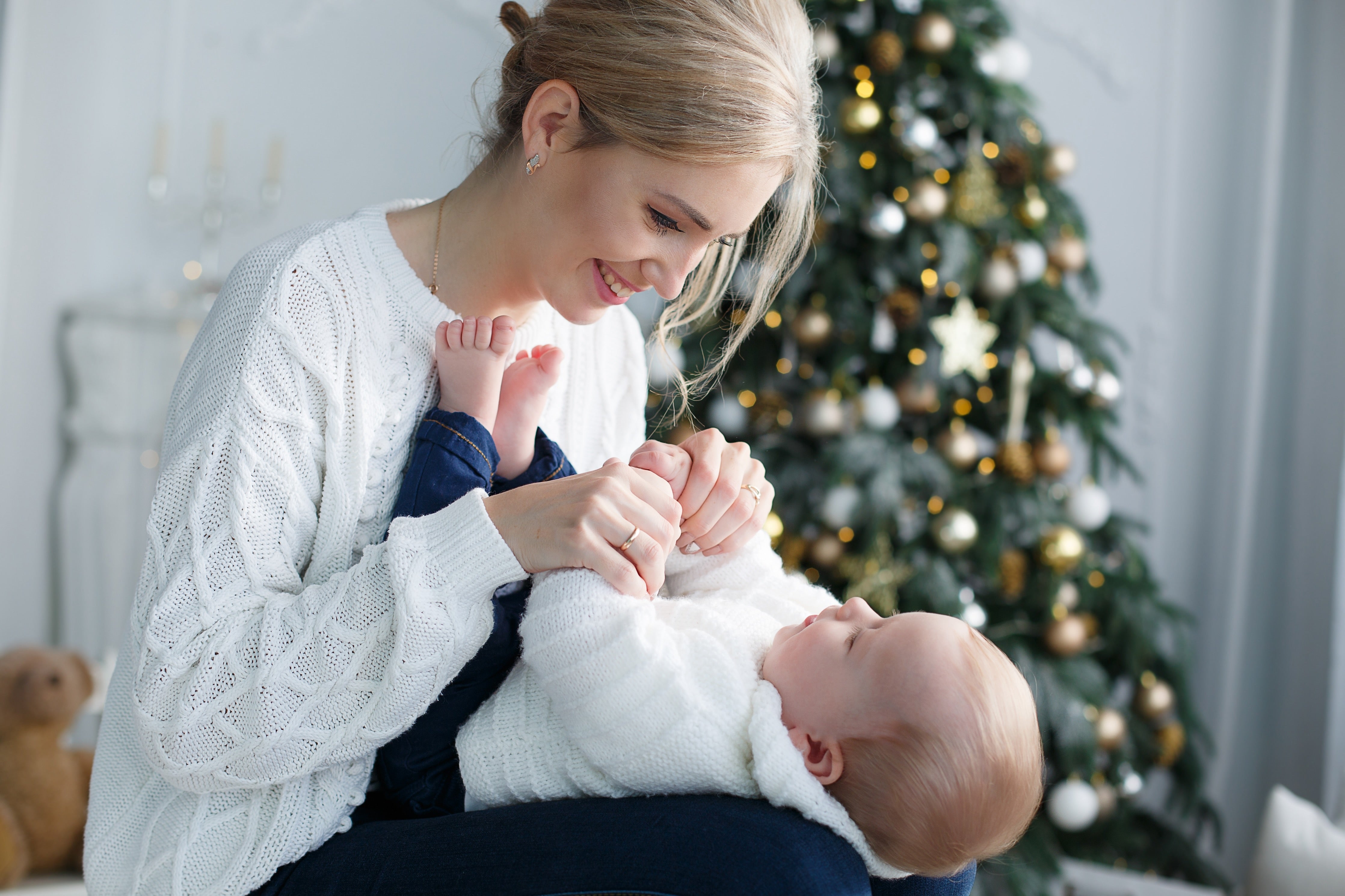 Mutter hält ihr Neugeborenes in einer ruhigen, weihnachtlichen Umgebung – Darstellung von Nähe und Geborgenheit.